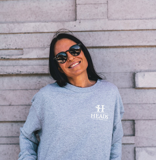 Girl smiling wearing a grey Heads of Noosa jumper with a white logo on the front 